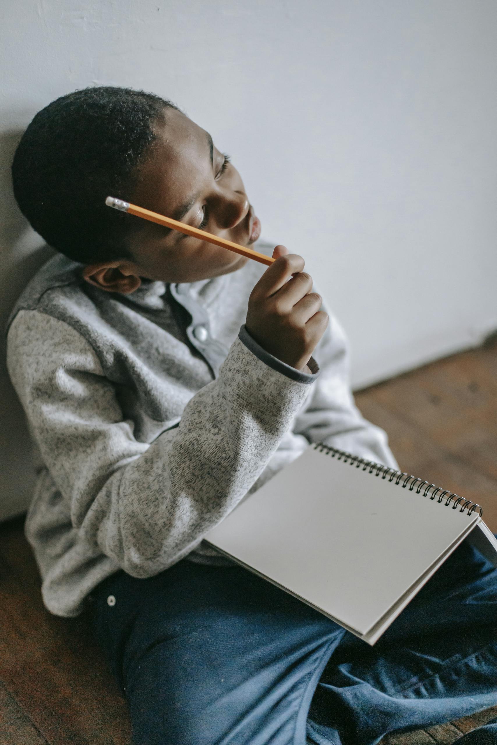 A young boy pondering with a pencil and notebook, suggesting education and creativity.