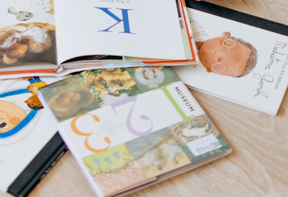 A cute child engaged in reading colorful books while sitting on a wooden floor indoors.